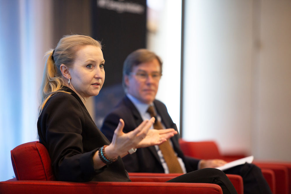 Anne White in foreground with Robert Stoner in the background on stage, seated, seakig gesturing with arms, MIT