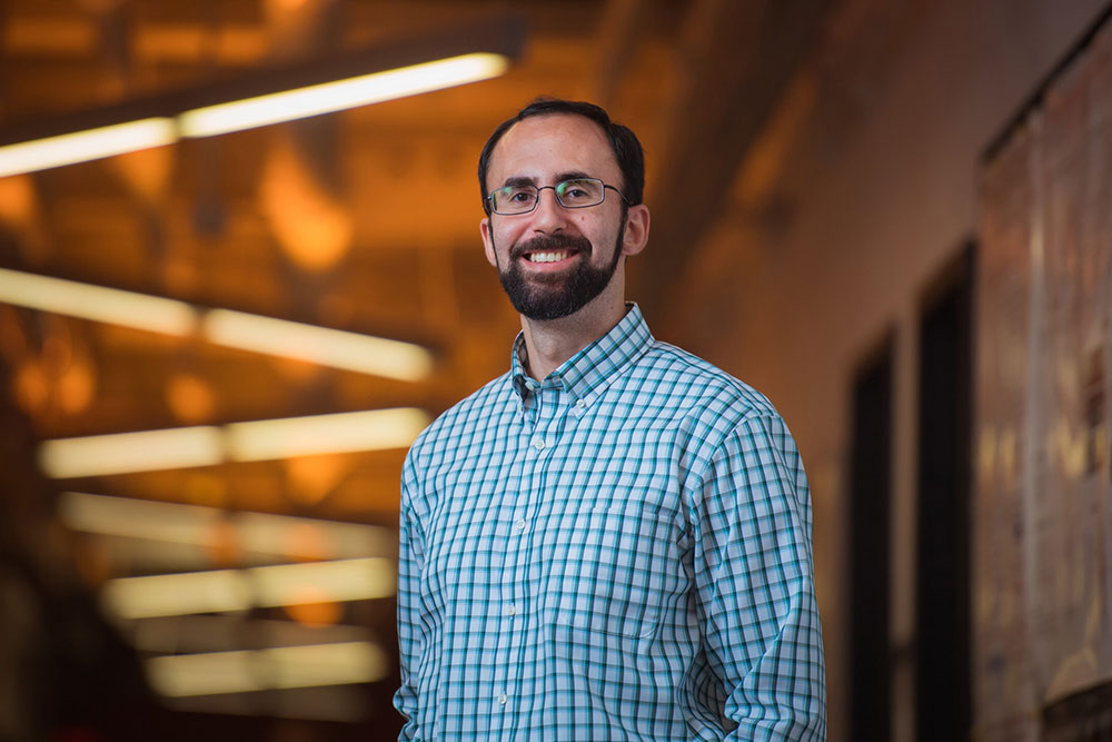 Faculty member Koroush Shirvan in a hallway with lighs overhead in a zig-zag pattern, MIT