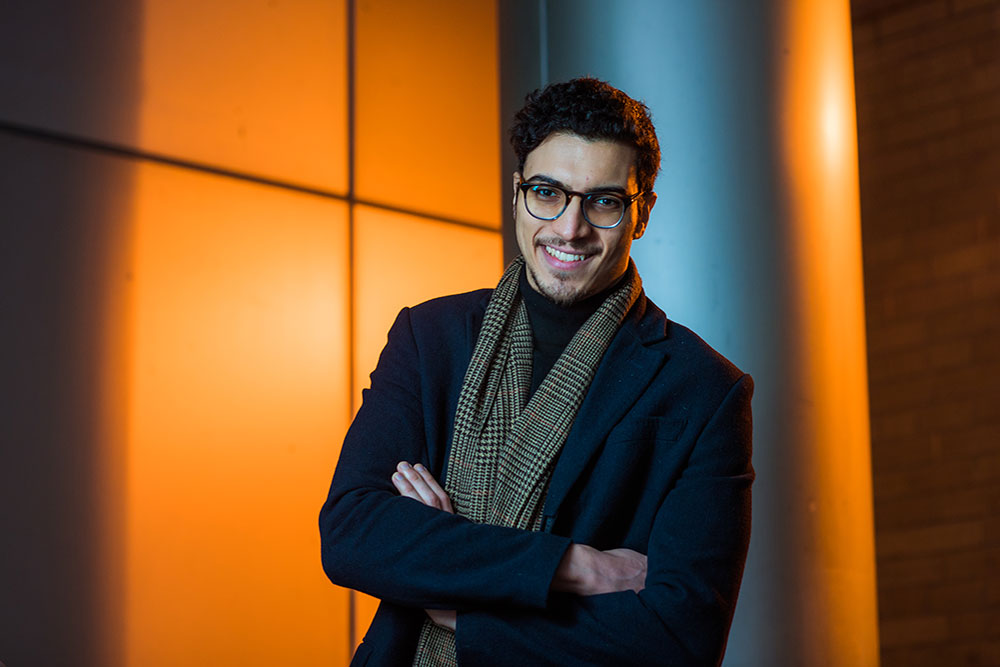 Male student standing against an orange background, MIT