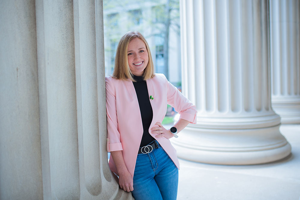 female leaning agains an architechtural column outdoors at MIT with left hand on hip