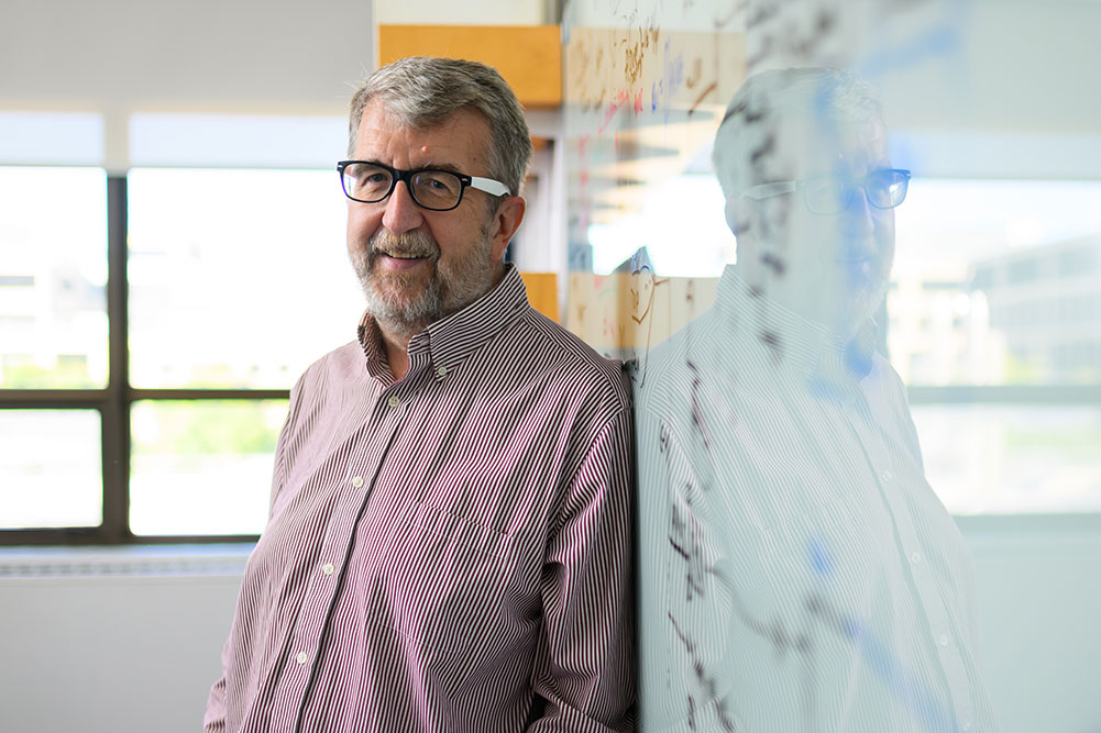 Faculty member Curtis Smith leaning on a glass whiteboard with writing inside and office with a window in the background, MIT