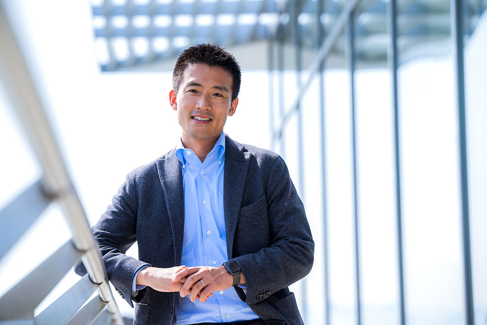 Alumnus, Masashi Hirose facing camera, blurred steel architectural features to the right and background, MIT