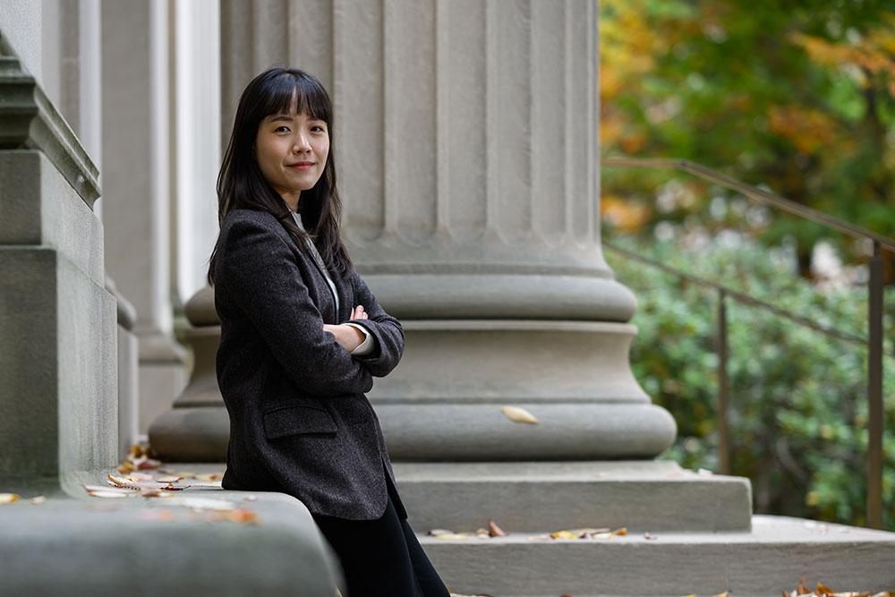 Graduate  student Youyeon Choi, arms folded outside on a path with trees on the right.