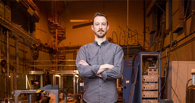 Faculty member Zachary Hartwig stands arms folded inside a lab space at MIT