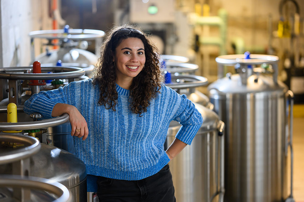 Graduate  student, Zoe Fisher, in a lab sapce with stainless steel dewars/tanks in the background